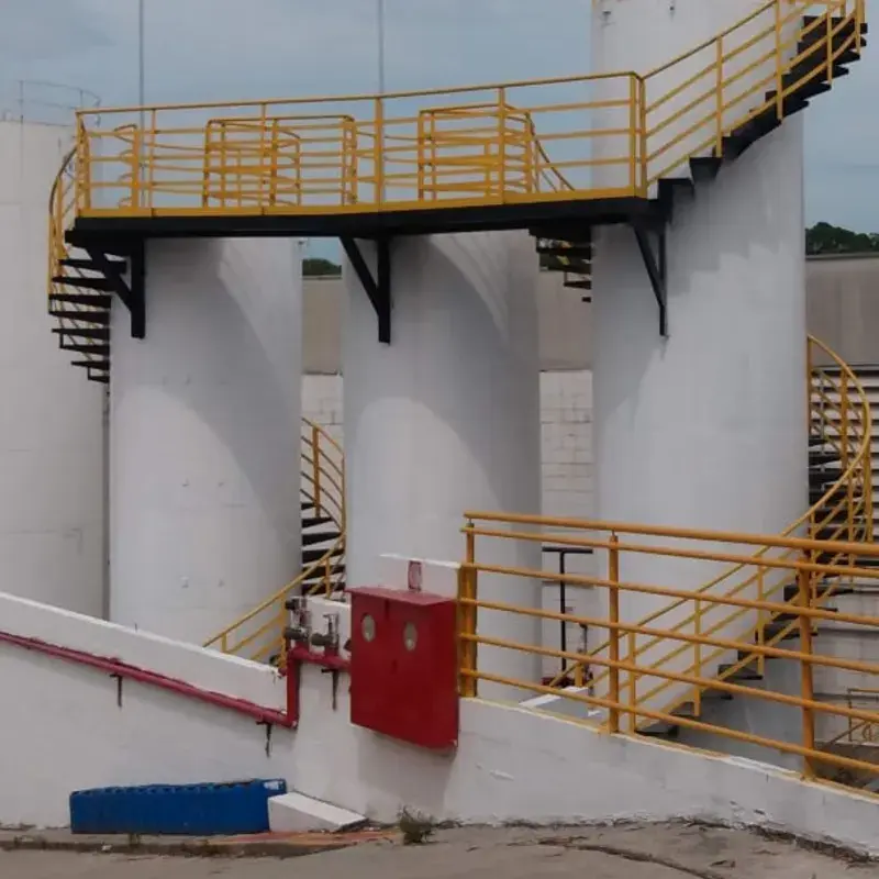 Plataforma operacional com guarda-corpo amarelo e acessos por escada entre tanques de armazenamento